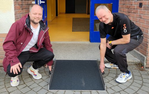 An der Turnhalle der Gesamtschule „Bruno H. Bürgel“ demonstrieren die Sportlehrer Herr Tilp und Herr Otto die neue Schwellenrampe.