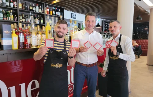 Bürgermeister Jörg Zietemann (Mitte) und die Gebrüder Mustafa, Geschäftsführer des Restaurants „Due Fratelli“ in Rathenow, präsentieren die neuen Veranstaltungsbierdeckel der Stadt Rathenow 